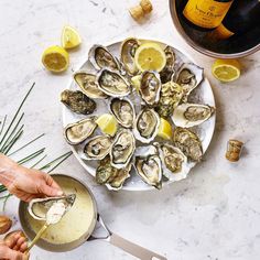 a plate full of oysters on a table next to some wine and lemon wedges