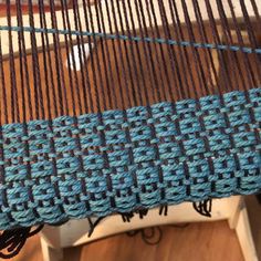 a close up view of a blue and brown weaving on a wooden table with two chairs in the background