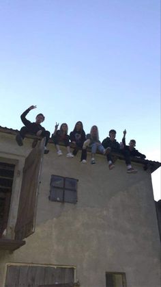 several people are sitting on the roof of a building and waving at something in the air