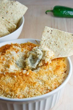 a white bowl filled with cheese and crackers on top of a table next to a green chili pepper