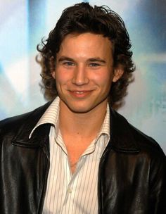 a young man in a leather jacket smiling at the camera