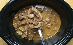 a spoon in a bowl filled with meat and gravy on top of a wooden table