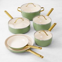 four green pots with gold handles and one white bowl on the side, all in different colors