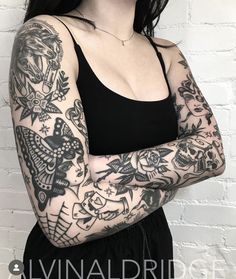 a woman with tattoos on her arms and chest standing in front of a brick wall