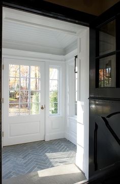 an open door leading to a white room with two windows and a gray tile floor