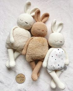 three crocheted stuffed animals laying next to each other on a white sheet with a button