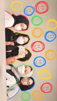 three young women standing in front of a wall with circles on it and one holding a cell phone