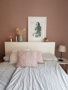 a bed with white sheets and pink pillows on top of it next to a lamp