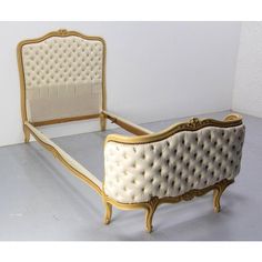 an old fashioned bed with gold trimmings and white upholstered headboard