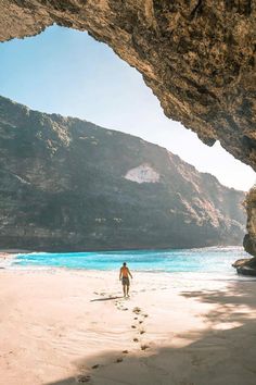 a man is walking on the beach in front of a cave