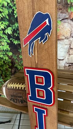 a wooden sign with the buffalo bills on it sitting next to a football and tree