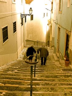 two people are walking down an alleyway with stone steps leading up to the door