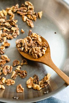 walnuts are being cooked in a frying pan with a wooden spoon on the side