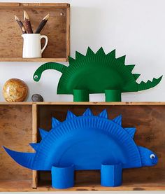 two cardboard dinosaurs are sitting on wooden boxes with pencils and paper machons in them