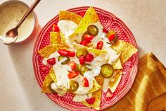 a red plate topped with nachos next to a bowl of ranch dressing