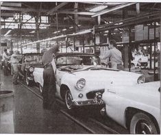 men working on cars in a factory with one man standing next to the car and another man looking at it