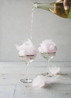 someone pouring champagne into two wine glasses filled with cotton floss