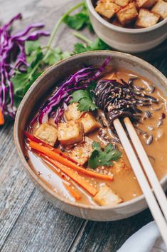 two bowls filled with food and chopsticks on top of a wooden table next to some veggies