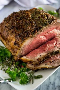 a piece of roast beef on a plate with parsley garnish and herbs