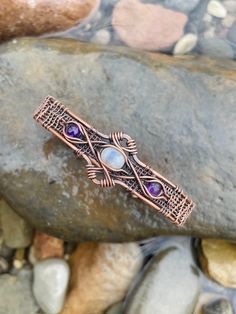 a copper bracelet with amethorate and purple stones on it sitting on some rocks