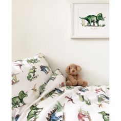 a stuffed animal sitting on top of a bed next to a wall mounted dinosaur print