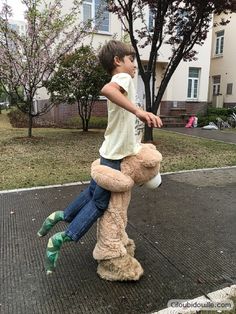 a young boy sitting on top of a teddy bear in the middle of a park