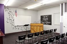 an empty room with chairs and a podium in front of a whiteboard on the wall