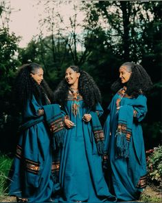 three women in blue dresses standing next to each other with trees in the back ground