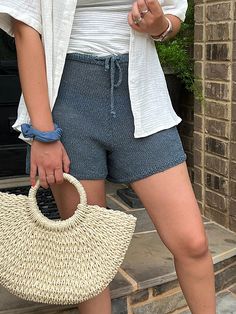 a woman is holding a straw bag and looking at her cell phone while standing in front of a brick building