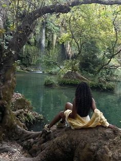 a woman sitting on top of a rock next to a river