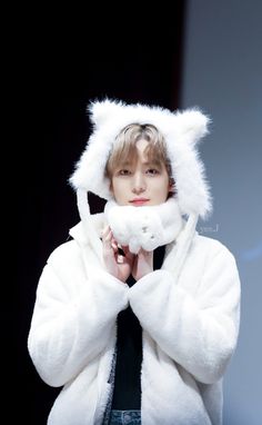 a young man wearing a white bear suit and holding his hands to his face while standing in front of a black background