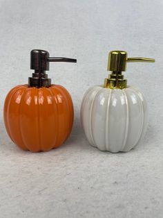 two pumpkin shaped soap dispensers sitting next to each other on a white surface