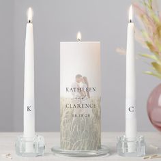 three candles with the names of two people on them and one candle in front of it