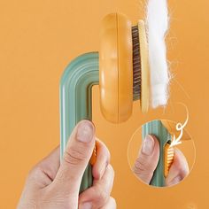 a hand holding a brush and comb over a hair dryer on an orange background