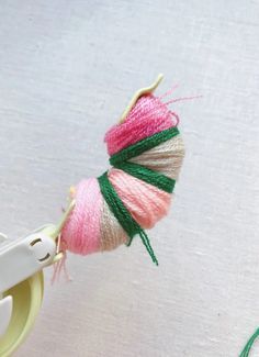 a pair of scissors and some yarn on a white tablecloth with a pink, green and beige ball of yarn