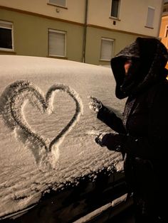 a person standing next to a car covered in snow with a heart drawn on it