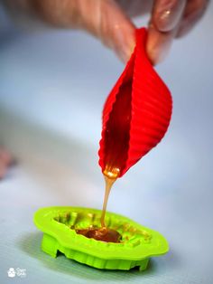 a person is pouring sauce into a green plastic container with a red paper fan on top