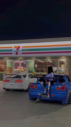 a woman sitting on the back of a blue car in front of a gas station