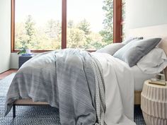 a bed with two pillows and blankets on top of it next to a large window