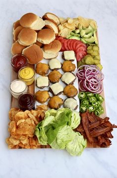 an assortment of food is laid out on a cutting board, including burgers, lettuce, tomatoes, and other foods