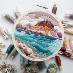 an embroidery project with mountains and water in the background, surrounded by small wooden pegs