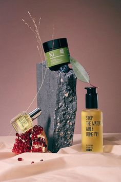 two bottles of skin care sitting next to each other on top of a rock and some berries