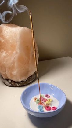 a small bowl with buttons in it next to a rock and incense stick on a table