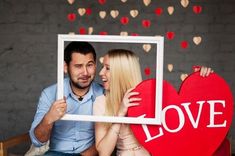 a man and woman holding up a heart shaped photo frame