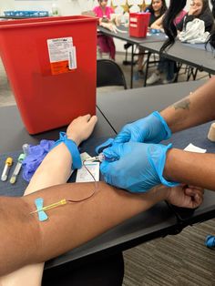 a woman getting her arm wrapped up with blue gloves and an iv in front of a red box