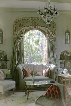 a living room filled with furniture and a chandelier hanging from the ceiling over a window