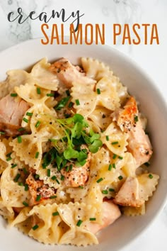 a white bowl filled with pasta covered in chicken and parsley on top of a marble table