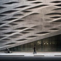 a woman walking down the street in front of a building that has wavy lines on it