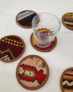 four woven coasters on a table with a glass in the middle and several different designs