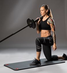 a woman squatting on a yoga mat holding a barbell